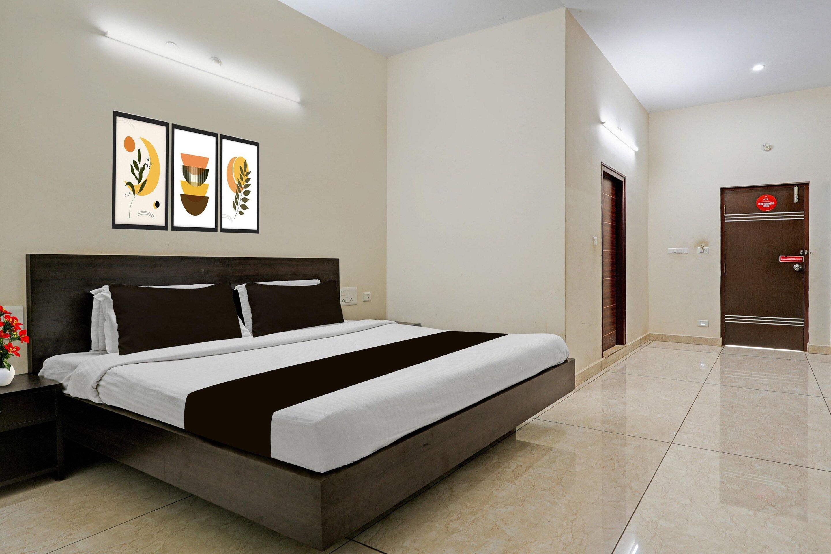 Camera d'albergo con un letto grande, un comodino con un vaso di fiori e una porta con il cartello 'No Smoking'.