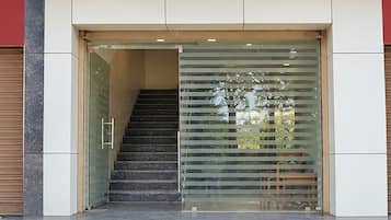 Een modern gebouw met een glazen deur, een trap die naar binnen leidt, en een metalen leuning aan de rechterkant.