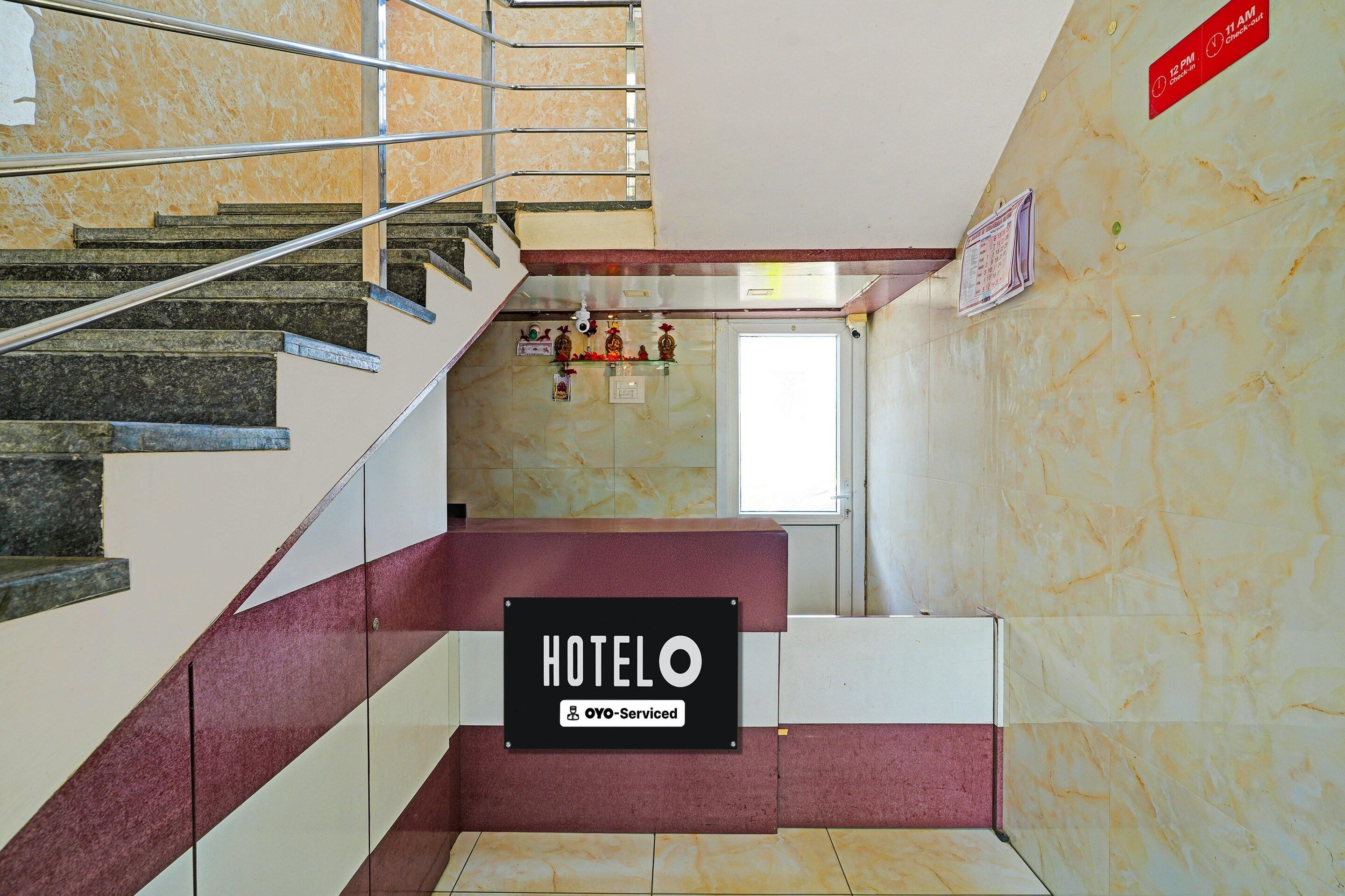 A hotel lobby with a marble staircase, a check-in/out sign, and a sign indicating OYO-Service.