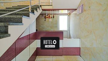 A hotel lobby with a marble staircase, a check-in/out sign, and a sign indicating OYO-Service.