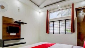 Una habitación de hotel con cama, televisor montado en la pared y una ventana con cortinas.