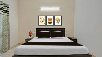 A hotel room with a bed, a nightstand, a phone, and a wall-mounted light. There are three framed pictures on the wall.