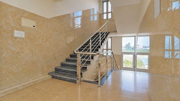 A spacious interior with a marble wall, a staircase with metal railings, and a large window providing a view of the outdoors.