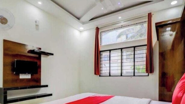 Habitación de hotel con cama, televisión instalada en la pared y ventana con cortinas.
