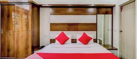 A hotel room with a large bed, a wooden headboard, a wardrobe, and a mirror.