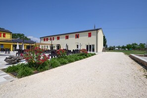 A building with a gravel driveway, outdoor seating area with tables and chairs, and a row of red-framed windows. - GuestHost - Kidane Room 3 Padova  (Padua)