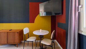 Ein Zimmer mit an der Wand montiertem Fernseher, einem Holzschrank, zwei Stühlen und einem kleinen runden Tisch.