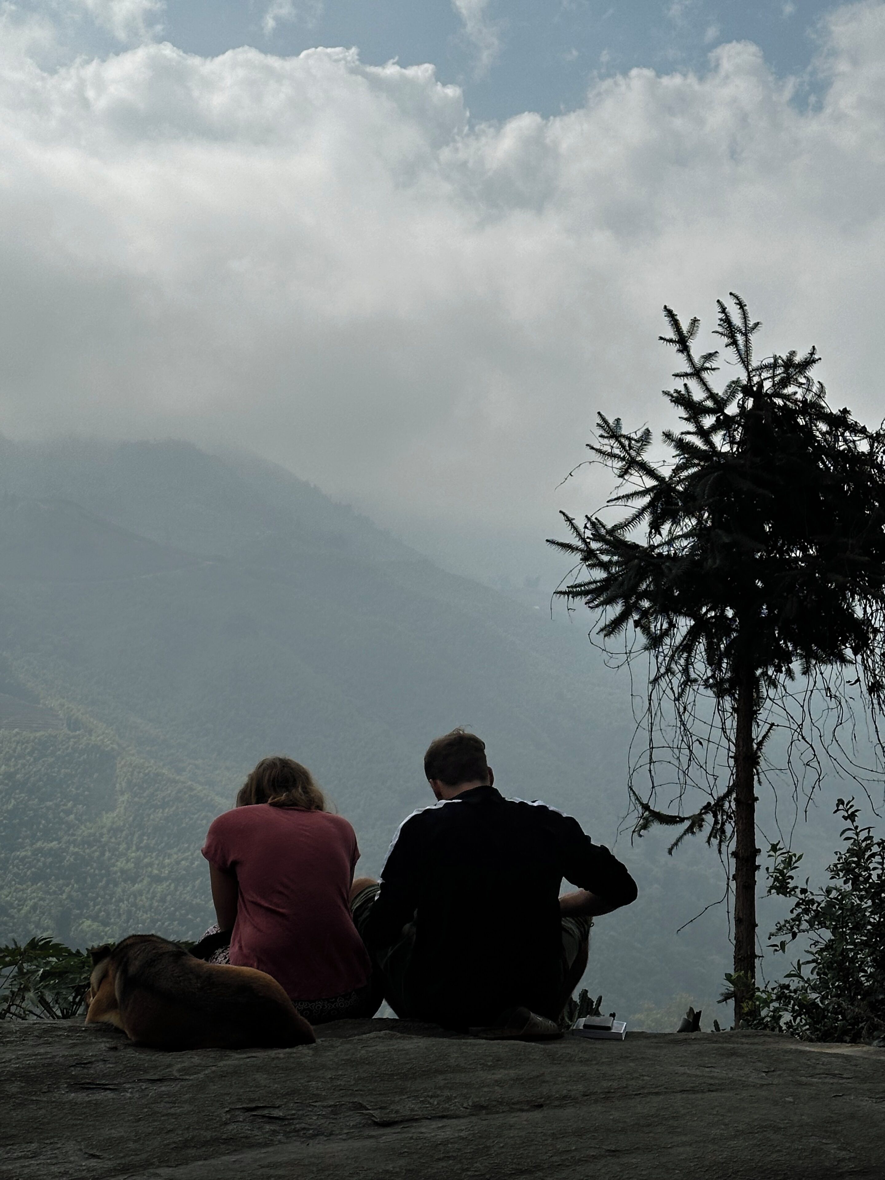 Two people sitting on a rocky outcrop overlooking a mountainous landscape.