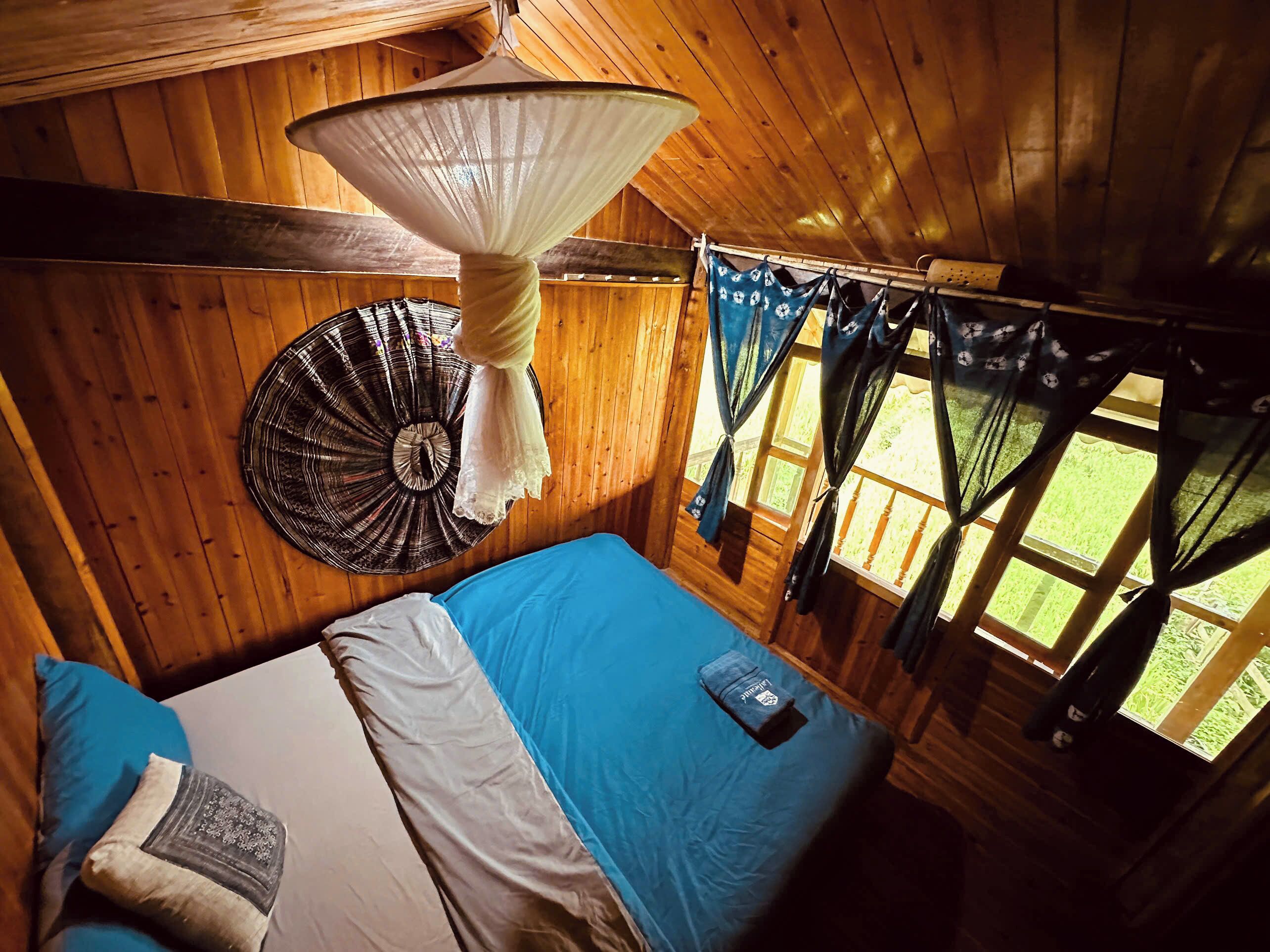 A wooden cabin room with a bed, a hanging mosquito net, and curtains.