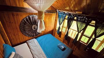 A wooden cabin room with a bed, a hanging mosquito net, and curtains.