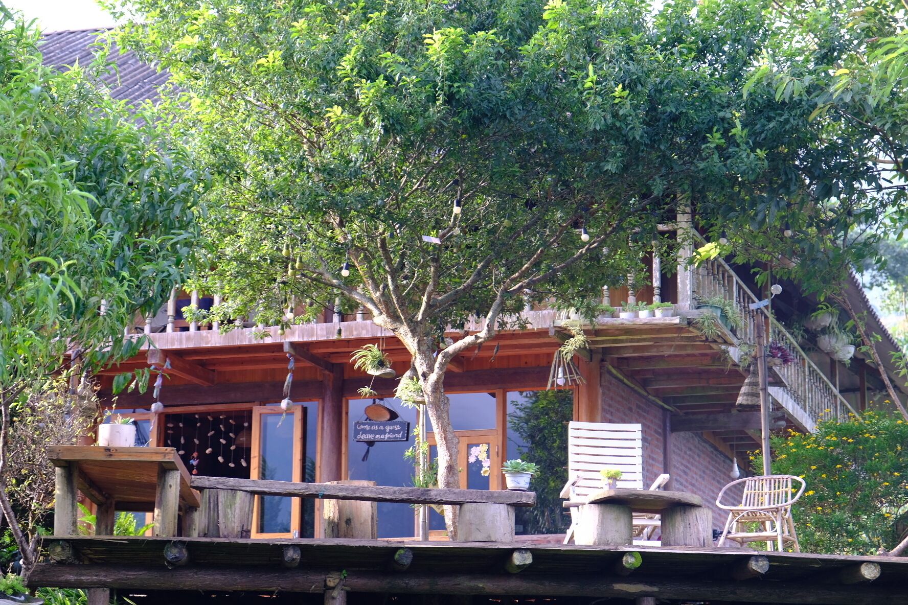 Un edificio de madera con balcón, una silla y plantas colgantes.