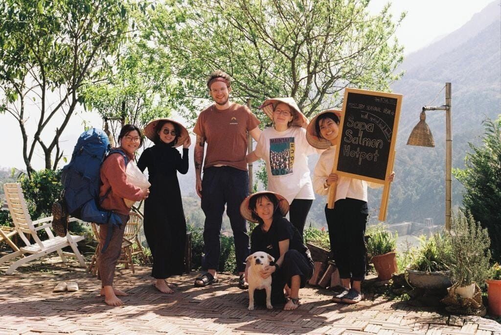 A group of people outdoors with a signboard displaying 'Sapa Salmon Hotpot'.