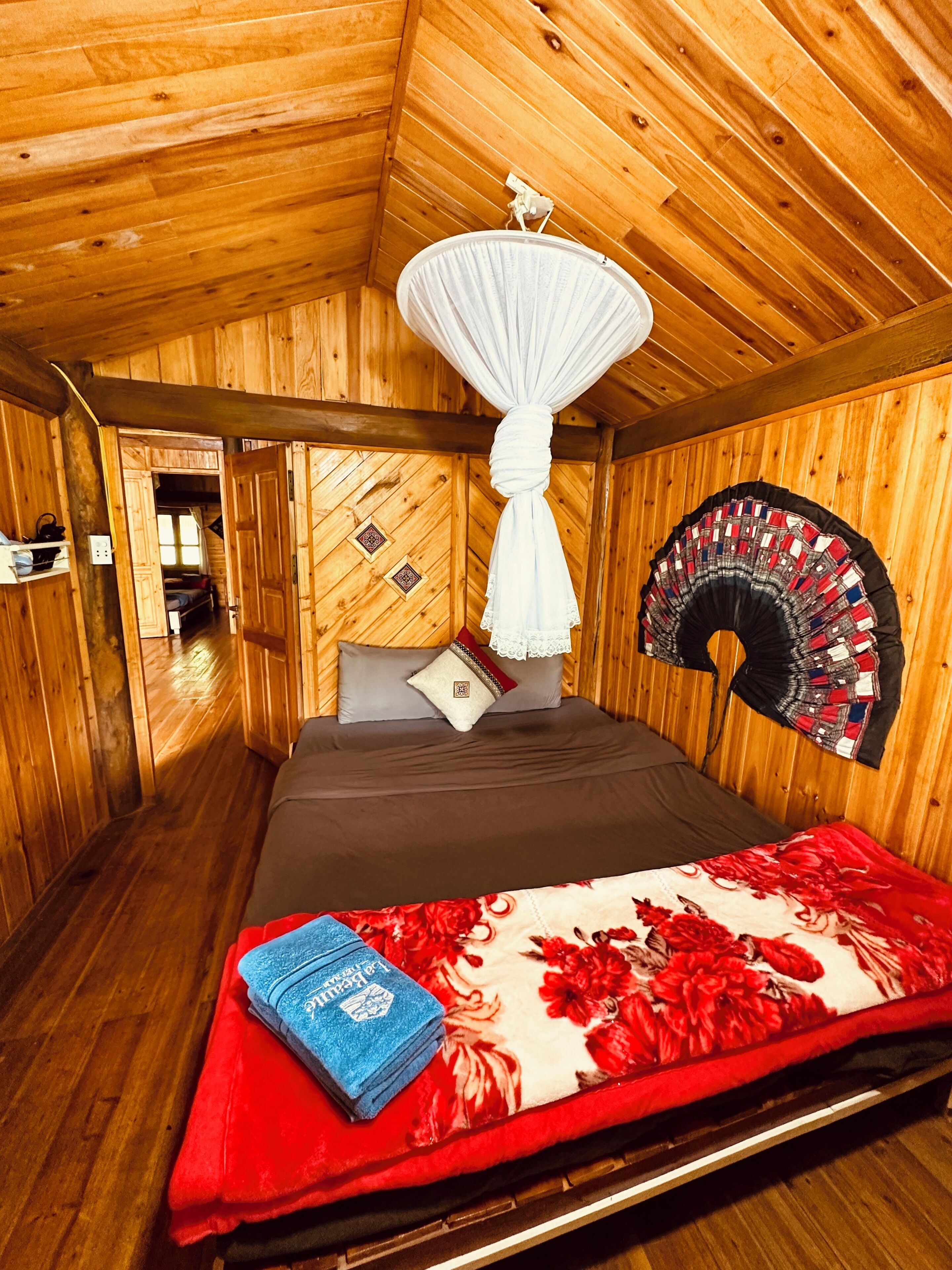 A wooden cabin room with a bed, a hanging mosquito net, and a decorative wall piece.