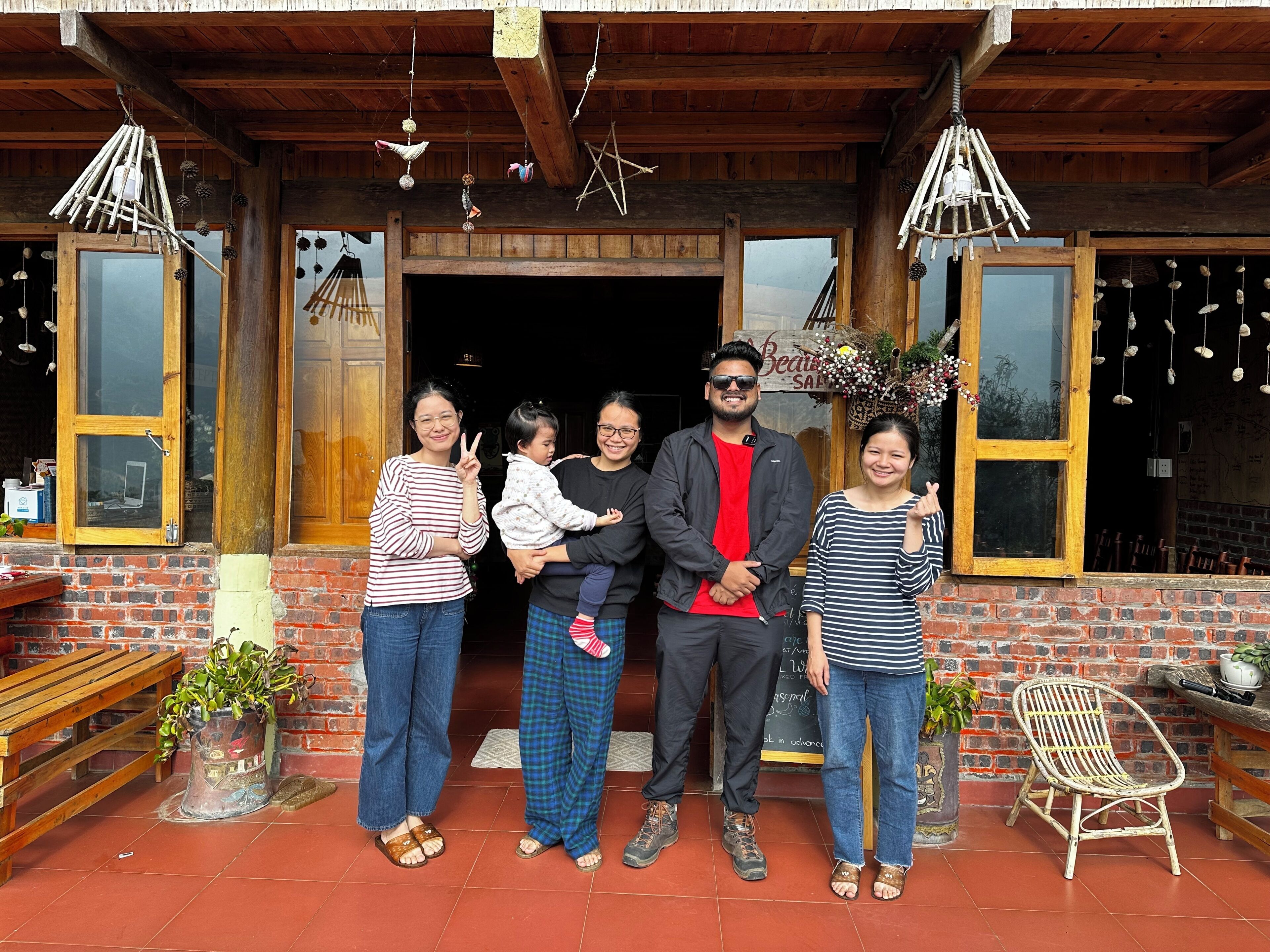 A family standing in front of a rustic building with a wooden facade, a bench, and a wicker chair.
