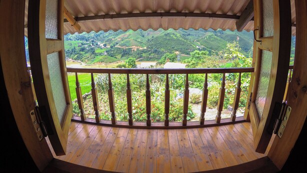 Un balcón de madera con vistas a colinas verdes y un río.