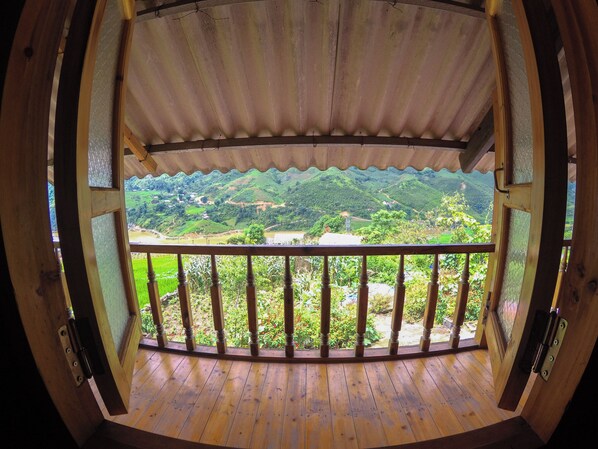 A wooden balcony with a view of green hills and a river.
