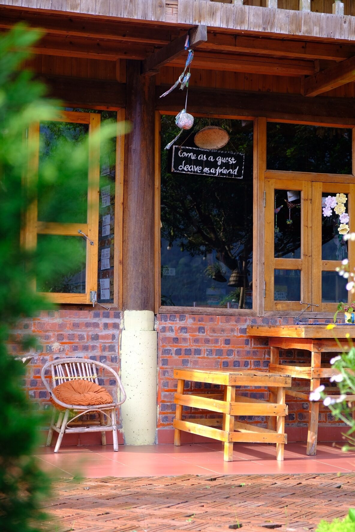 A wooden building with a sign that reads 'Come as a guest, leave as a friend.' There is a wicker chair and a wooden table outside.
