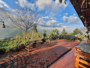 Un patio con suelo de ladrillo, muebles de madera y vistas a montañas y nubes.