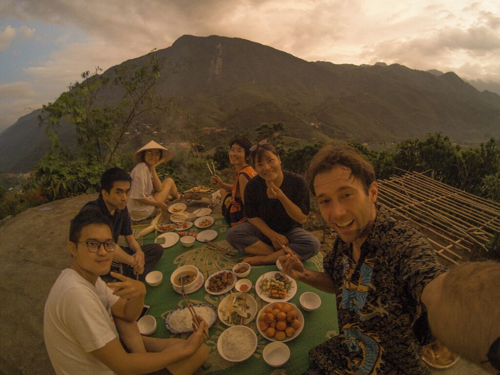 A group of people sitting around a table outdoors with a mountainous backdrop.