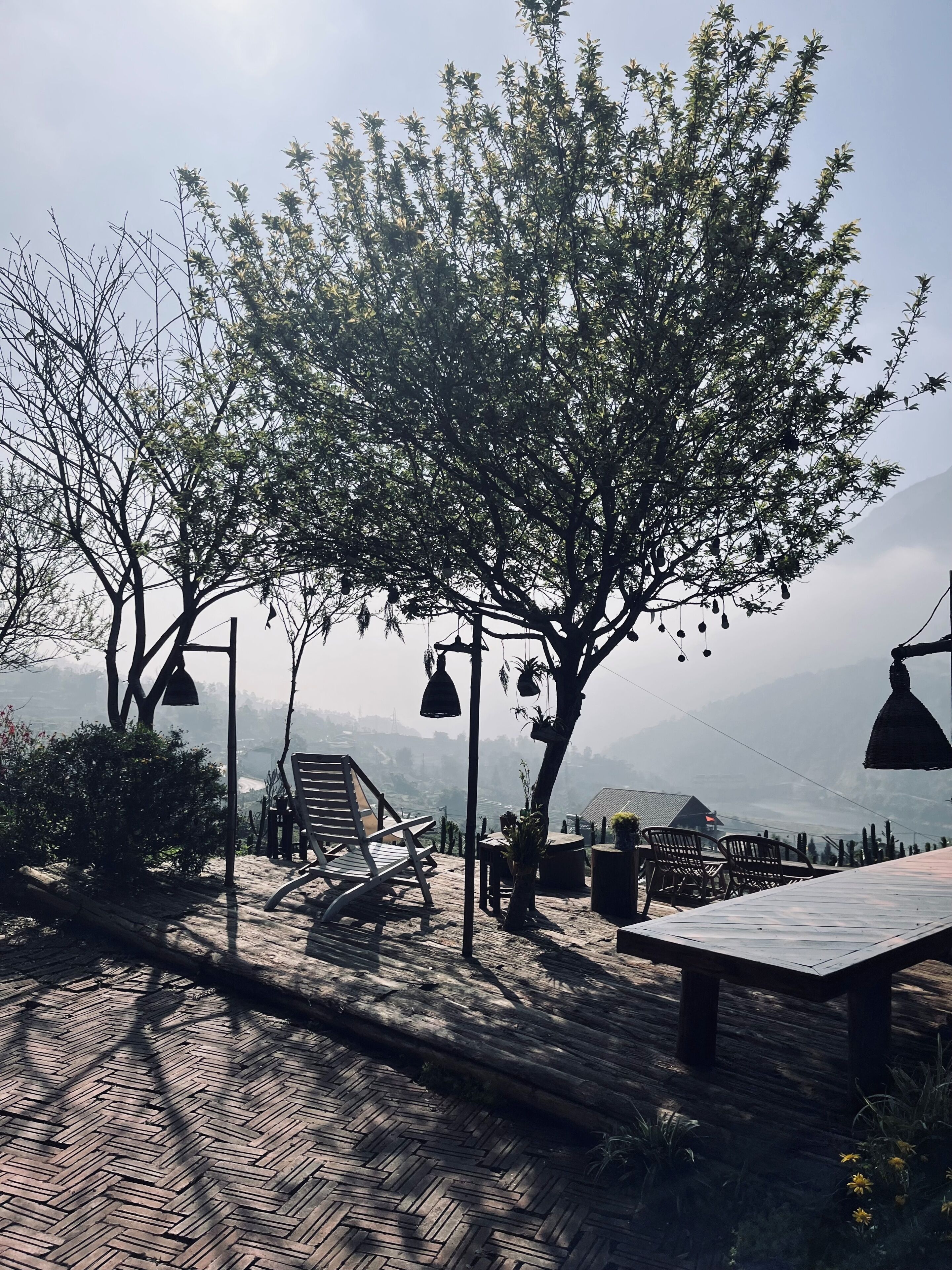 Un espace extérieur aménagé avec du mobilier en bois et des guirlandes lumineuses, offrant une vue sur un paysage montagneux.