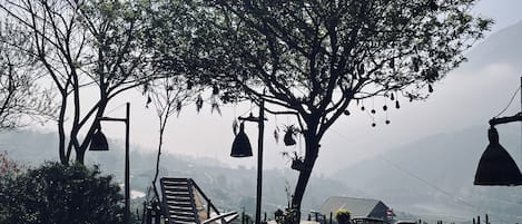 Uma área de estar ao ar livre com móveis de madeira e luminárias pendentes, com vista para uma paisagem montanhosa.