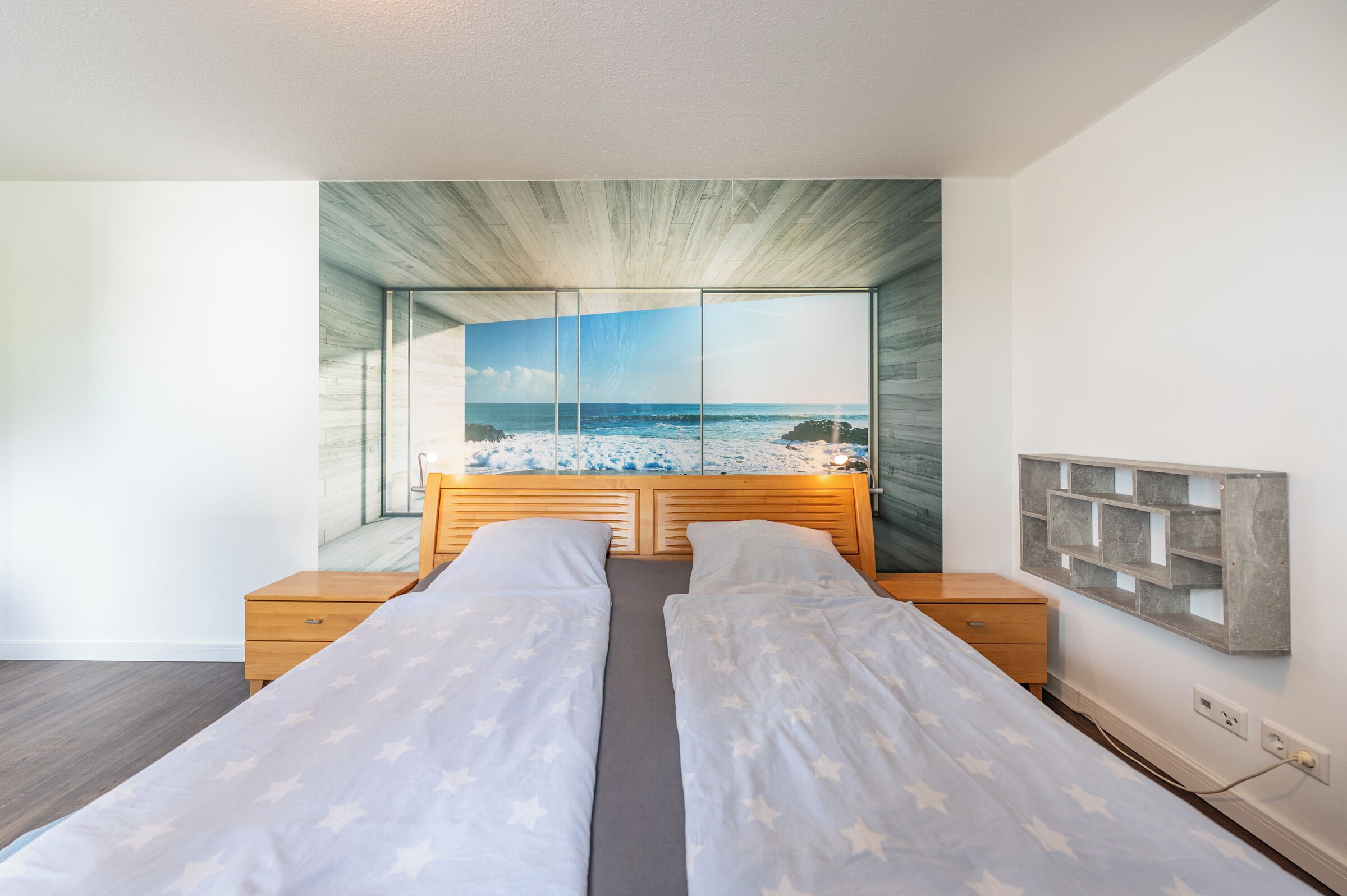 A bedroom with a large window, a bed with two pillows, a wooden headboard, and a nightstand.