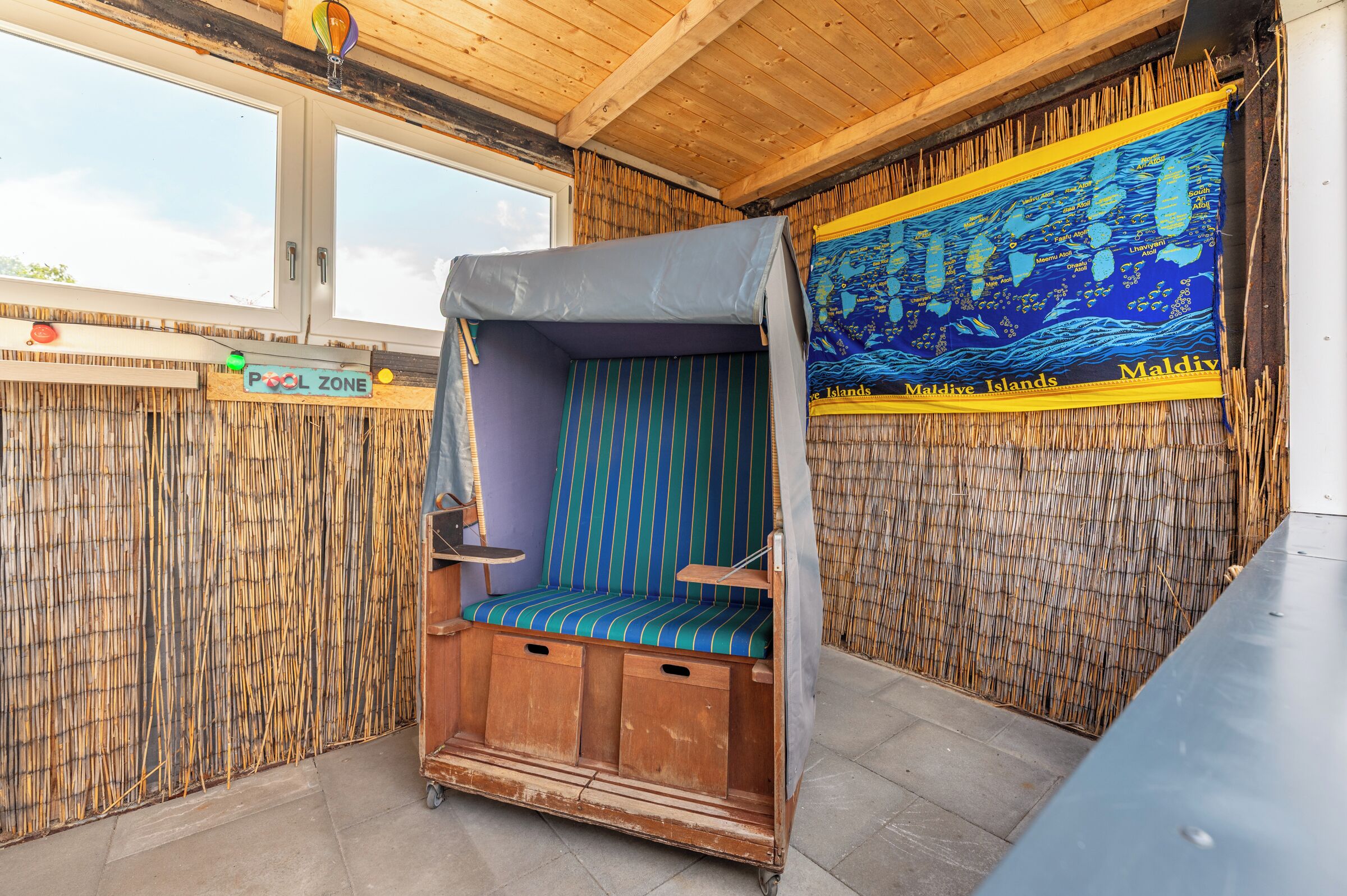 Ein Zimmer mit Holzboden, einem Fenster, einer Karte an der Wand, einer kleinen Holzbank und einer Bambuswand.