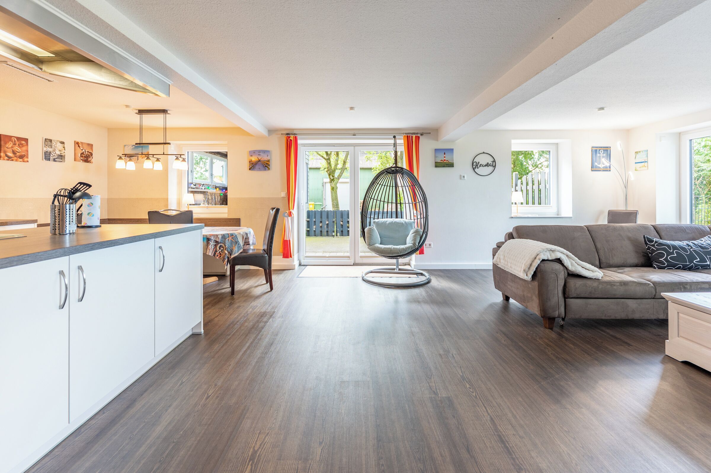 Ein modernes Wohnzimmer mit einer Couch, einem Essbereich mit Tisch und Stühlen, einem Hängesessel und einer Küche mit Schränken und einer Arbeitsplatte.