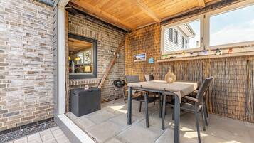 Eine Terrasse im Freien mit Backsteinwand, Holzboden und einem Tisch mit Stühlen.