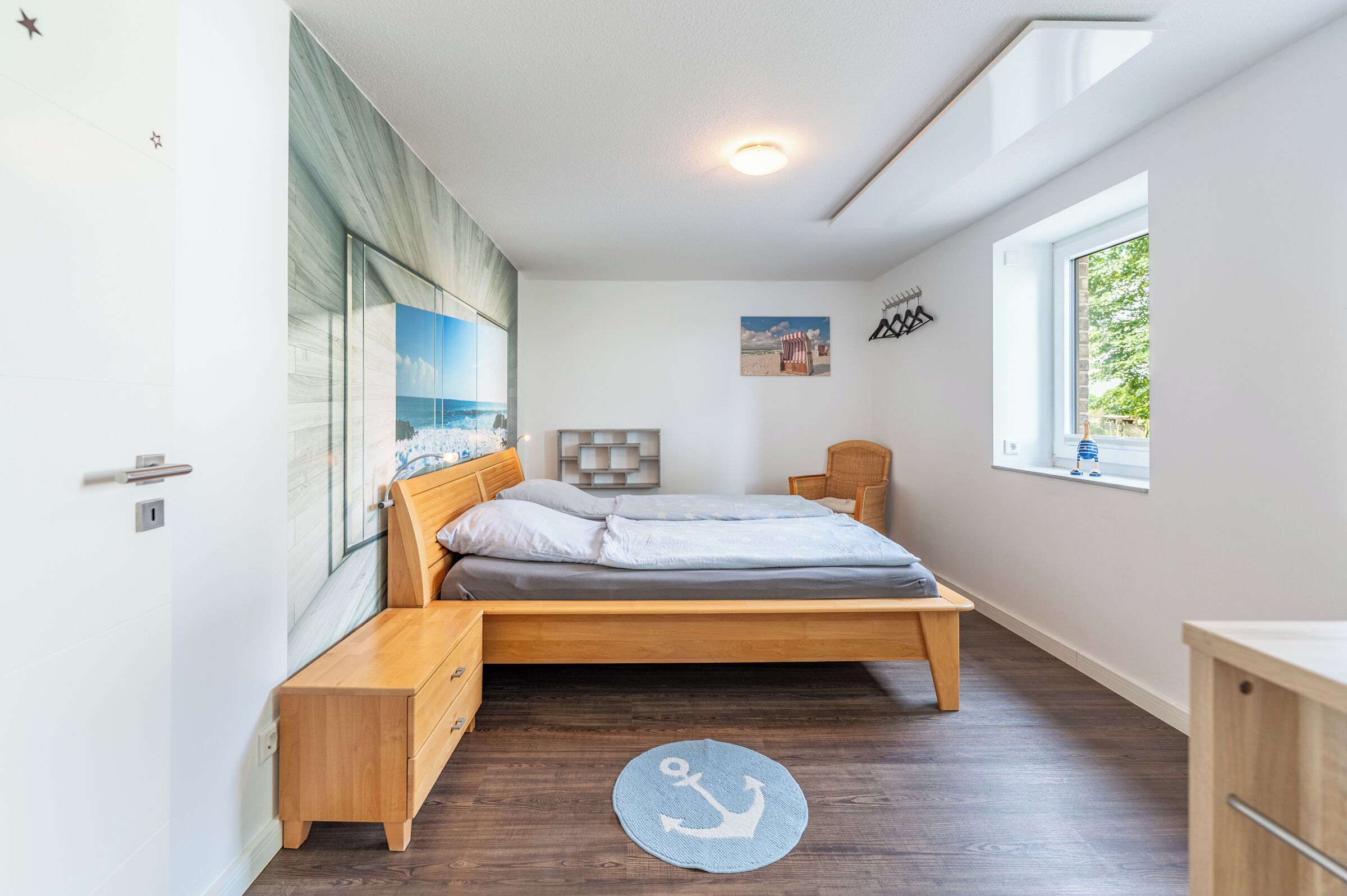 A bedroom with a bed, bedside table, a small chair, a window, and a picture on the wall.