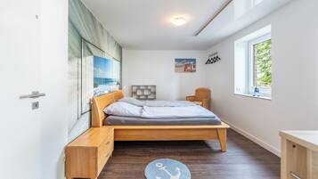 A bedroom with a bed, bedside table, a small chair, a window, and a picture on the wall.