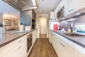 Une cuisine moderne équipée d’un four à micro-ondes, d’un four et d’un évier. Elle comprend un plan de travail en bois et offre une vue sur la buanderie.