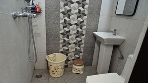 A small bathroom with a shower, a sink, a toilet, a decorative wall, and a trash bin.