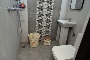 Un bany petit amb dutxa, un lavabo, un vàter, una paret decorativa i un cistellera.