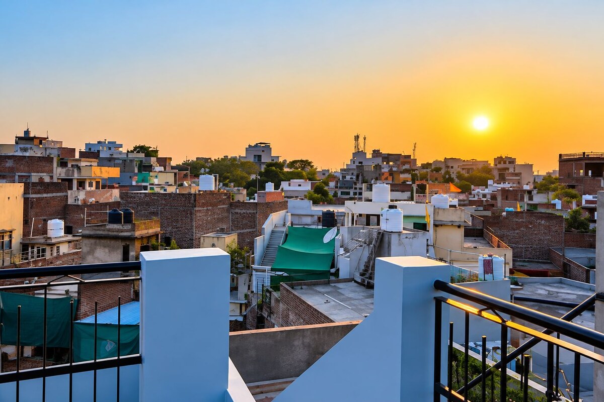 Paisaje urbano al atardecer con varios edificios, algunos con tanques de agua en los tejados, y un lona verde sobre una estructura.