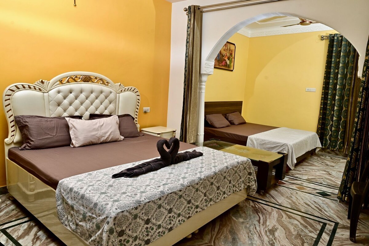 Una habitació d'hotel amb un llit gran, un llit més petit i una zona de seients. Hi ha un mirall a la paret i un quadre sobre el llit més petit.
