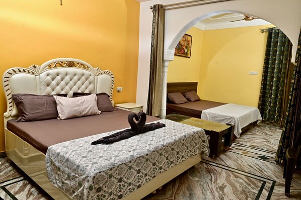 A hotel room with a large bed, a smaller bed, and a sitting area. There is a mirror on the wall and a painting above the smaller bed.