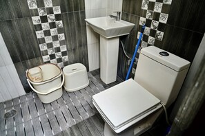 A bathroom with a white sink, toilet, and a bidet. There are two white buckets and a blue hose. The floor has a grey striped pattern.