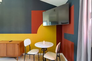 A room with a flat-screen TV mounted on the wall, a wooden cabinet, and two round tables with chairs. - GuestHost - Kidane Room 4 Padova (Padua)