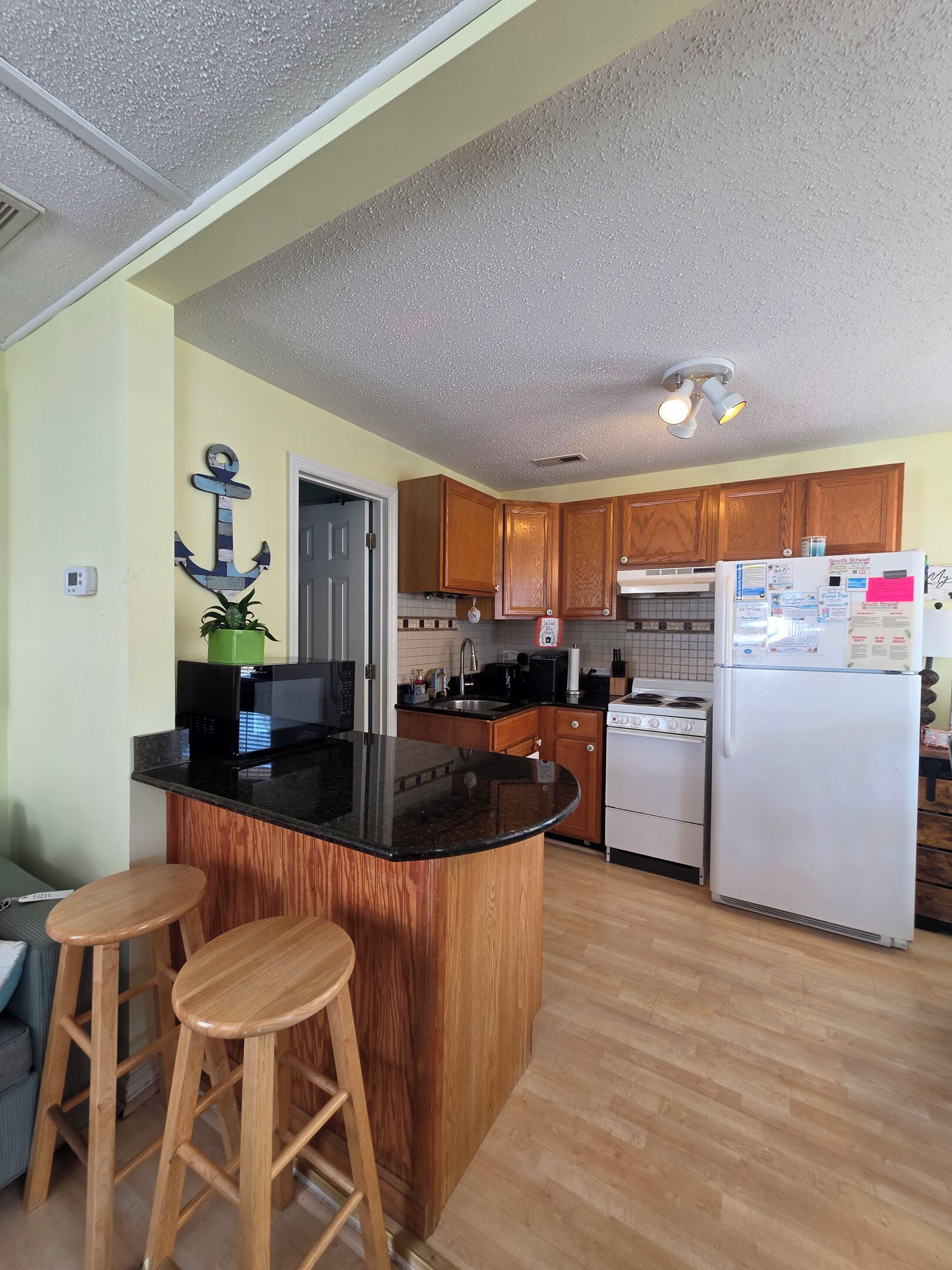 Una cocina con armarios de madera, encimera negra, refrigerador blanco y una isla de madera con taburetes.