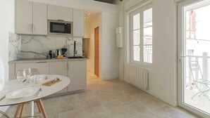 A modern kitchen with a built-in microwave, a dining table with chairs, and a view through a glass door to the outside. - 1bdr/3p Flat - Balcony - in the Heart of Deauville (Deauville)