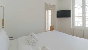 A hotel room with a large bed, a flat-screen TV mounted on the wall, and a window providing a view of the outside. - 1bdr/3p Flat - Balcony - in the Heart of Deauville (Deauville)