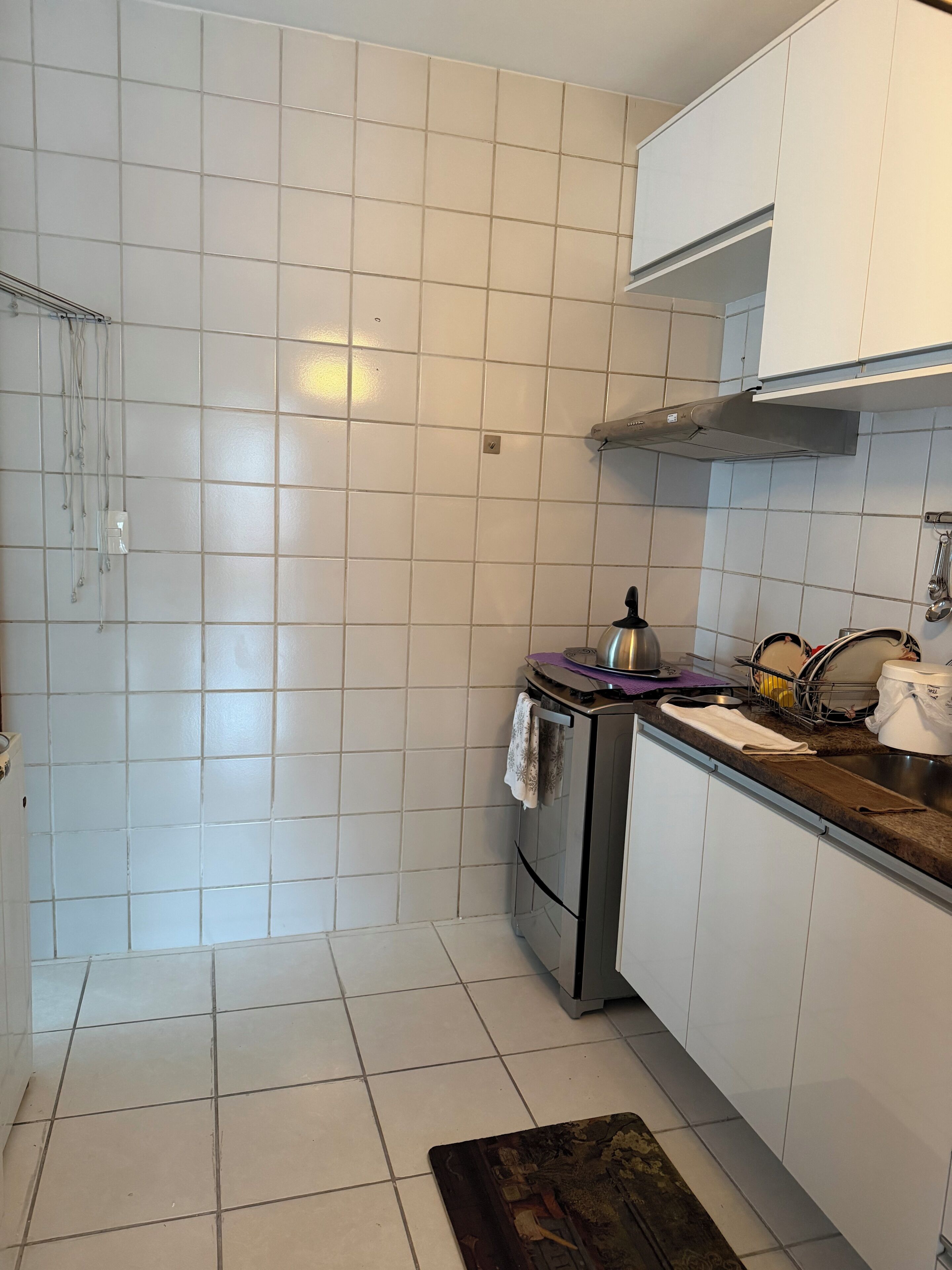 A kitchen with white tiled walls, a stainless steel range hood, and a dish rack.