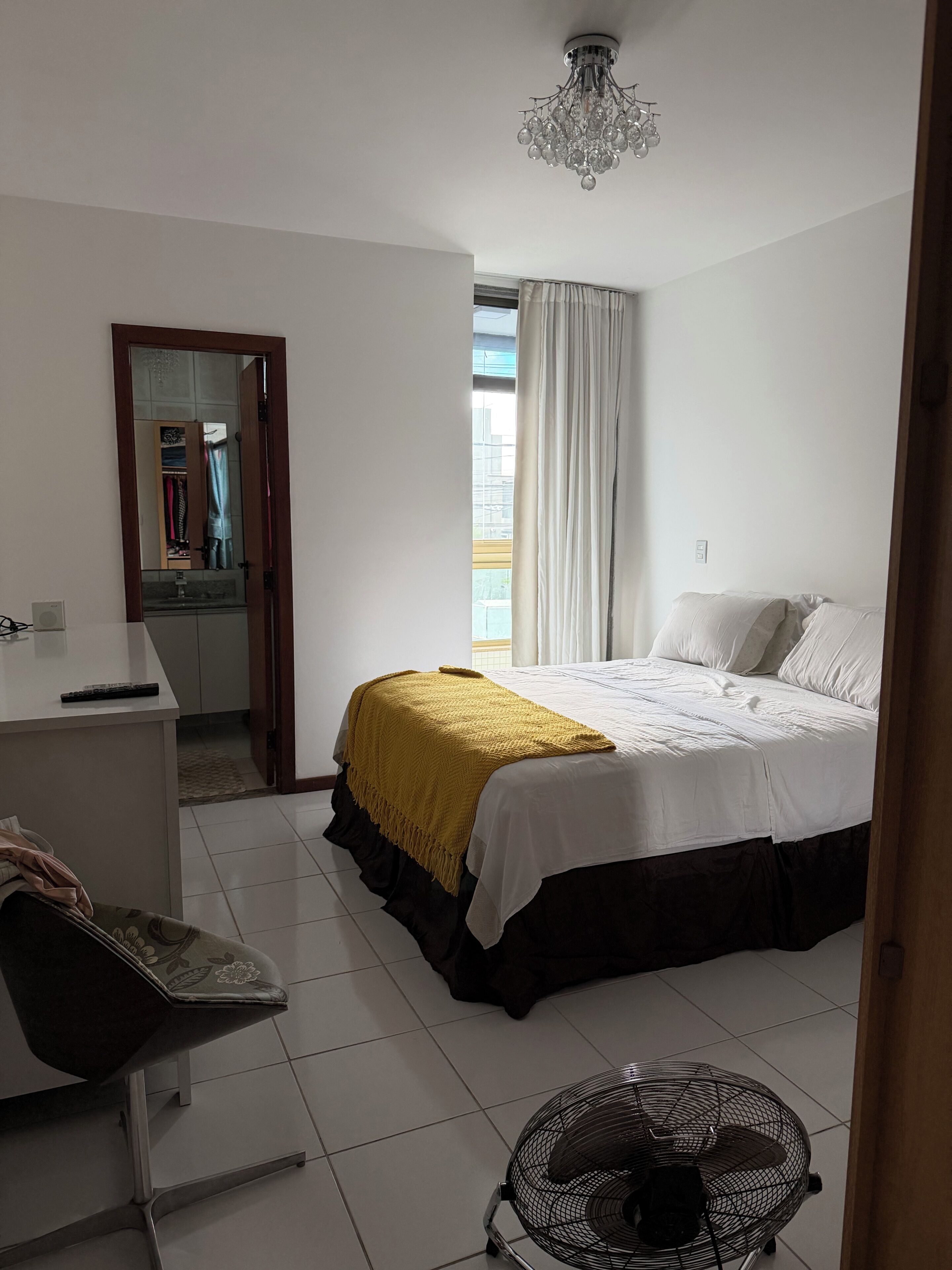 Habitación de hotel con cama, escritorio, silla, ventilador y vistas al exterior.