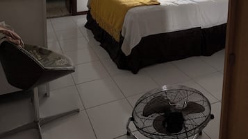 Quarto de hotel com cama, escrivaninha, cadeira, ventilador e vista para o exterior.