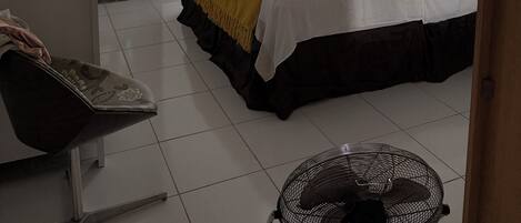 A hotel room with a bed, a desk, a chair, a fan, and a view of the outside.