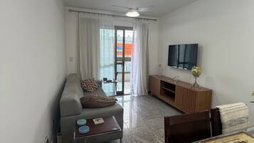 Uma sala de estar moderna com sofá, mesa de centro e uma televisão de tela plana na parede.
