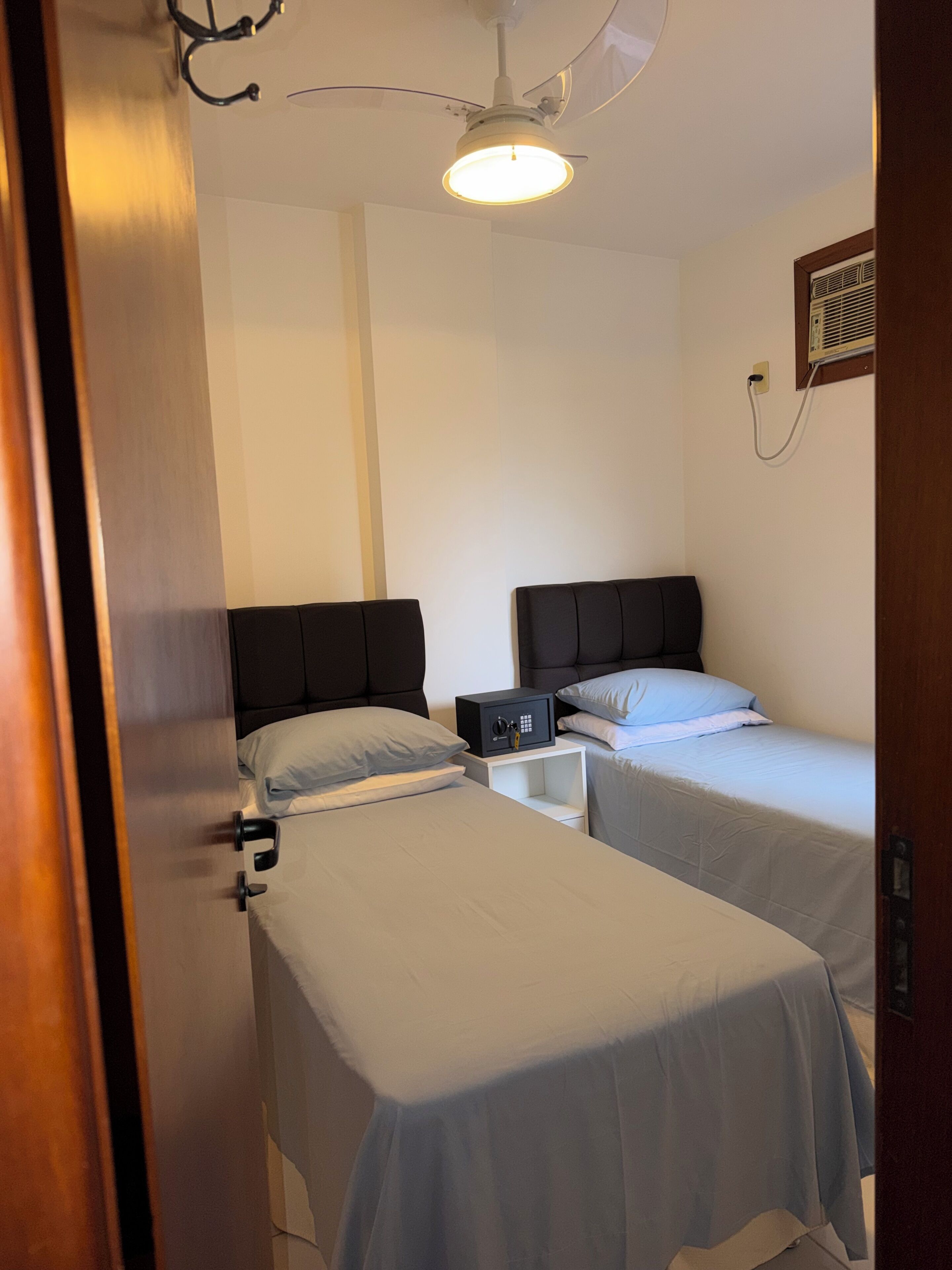 Ein Hotelzimmer mit zwei Einzelbetten, einem Nachttisch mit Lampe, einem Deckenventilator und einer Wand-Klimaanlage.