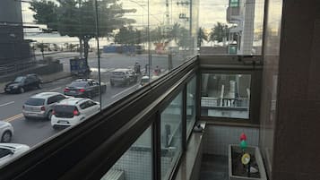 Uma varanda com vista para uma rua movimentada, piso de azulejos e um vaso de planta.