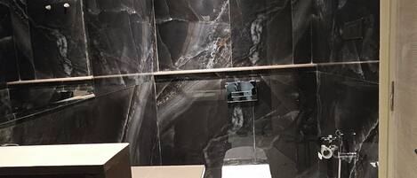 Een moderne badkamer met een marmeren spatwand, een wit toilet en een wastafelmeubel met spiegel.